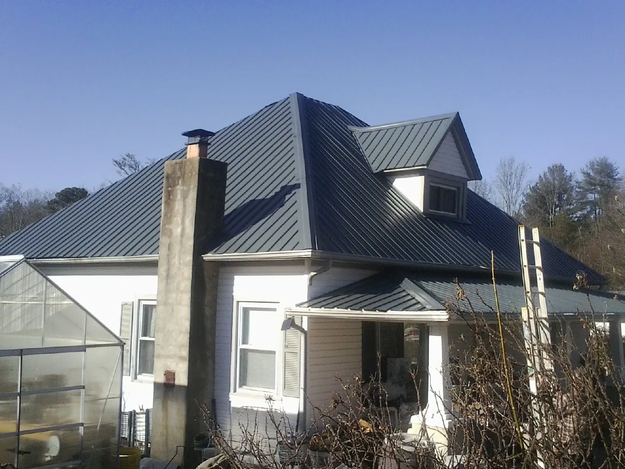 Dark blue standing seam metal roof on a white farmhouse with dormer — Slate & Tile Roof Repair by Roofing Brothers in Rock City Falls
