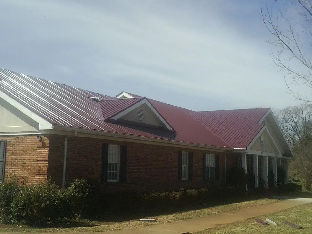 Red metal roof with gabled entries on a long brick building, from a Hail Damage Roof Repair job in Rock City Falls