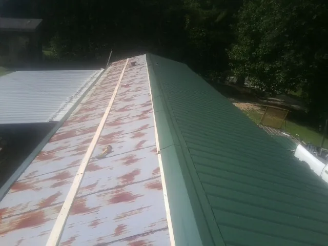 Old rusted panels beside newly installed green metal roofing — Wind Damage Roof Repair by Roofing Brothers in Rock City Falls