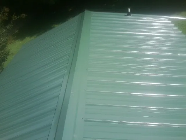 New green metal panels meeting at the ridge of a roof — Flat Roof Repair work by our crew in Rock City Falls