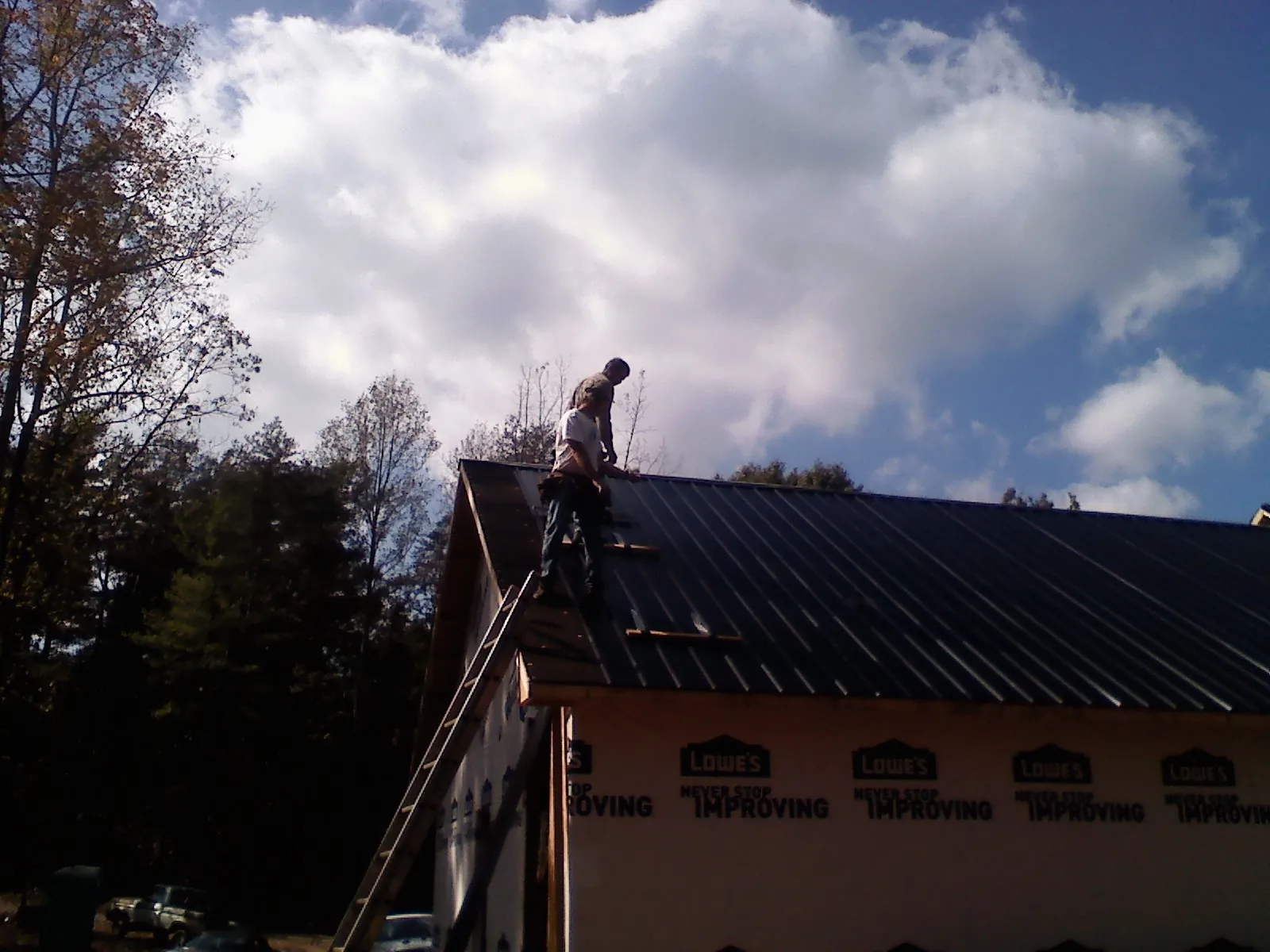 Roofer fastening dark metal panels high against a cloudy sky, from a Roof Inspection job in Rock City Falls