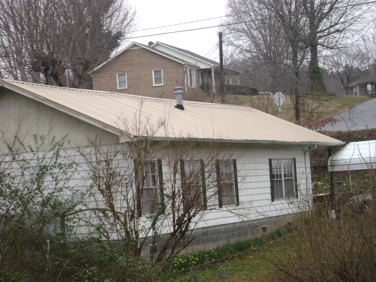 Tan metal roof on a white sided house set into a hillside — Commercial Roofing by Roofing Brothers in Rock City Falls